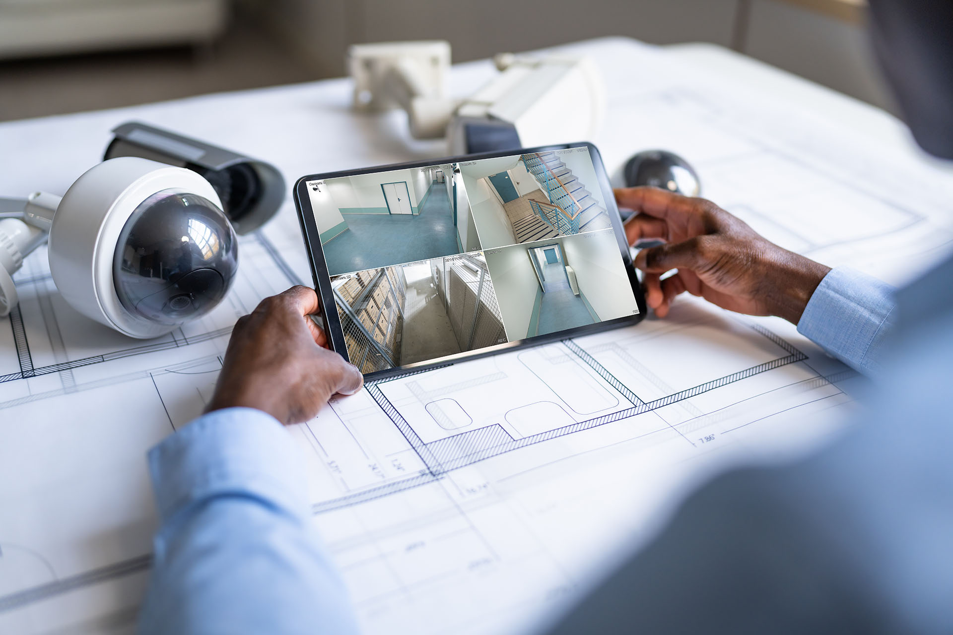 Tablet mit Überwachungskameras auf Bauplan neben Sicherheitstechnik
